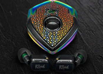 A pair of black Klipsch wireless earbuds with a jeweled, multi-colored triangular charging case on a dark textured surface—perfect for those seeking luxury accessories and a true style upgrade.
