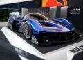 A sleek blue hypercar is displayed on a raised platform at an event, celebrating 75 Years of F1, with Red Bull Advanced Technology branding in the background.