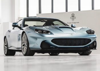 A light blue Touring Superleggera sports car with a sleek design is parked indoors on a white floor at a North American dealership, viewed from a low front angle.