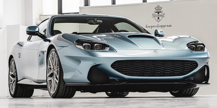 A light blue Touring Superleggera sports car with a sleek design is parked indoors on a white floor at a North American dealership, viewed from a low front angle.