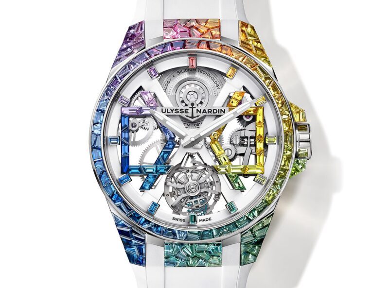 The limited-edition Ulysse Nardin Blast Sparkling Rainbow wristwatch features a white band, open-worked dial, and a bezel adorned with multicolored gemstones arranged in a radiant gradient pattern.