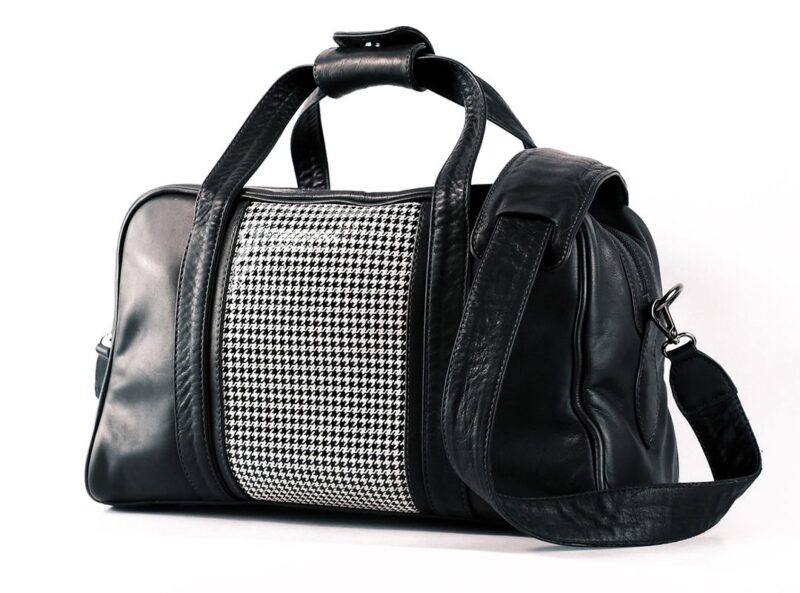 Black leather duffel bag with a houndstooth patterned panel in the center and an adjustable shoulder strap, featured in the duPont REGISTRY Father’s Day Gift Guide—perfect for those seeking stylish Father's Day gifts.