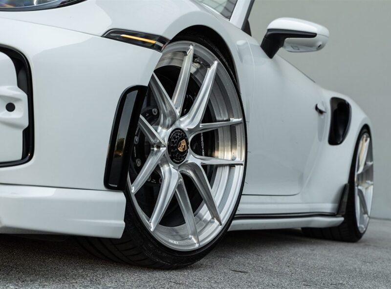 Close-up view of the front wheel and fender of a Porsche TechArt 911 Turbo S, featuring large silver ANRKY XR Wheels from Wheels Boutique and low-profile tires on a concrete surface.