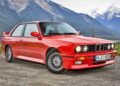A red BMW E30 M3 coupe parked on a gravel road, with important mountain views and lush greenery in the background.