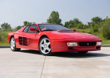 A rare Ferrari 512 TR Prototype sports car is parked on a driveway with greenery and trees in the background under a clear sky.