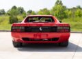 Rear view of a red Ferrari 512 TR pre-production prototype parked outdoors on a concrete surface, with green trees and grass in the background.