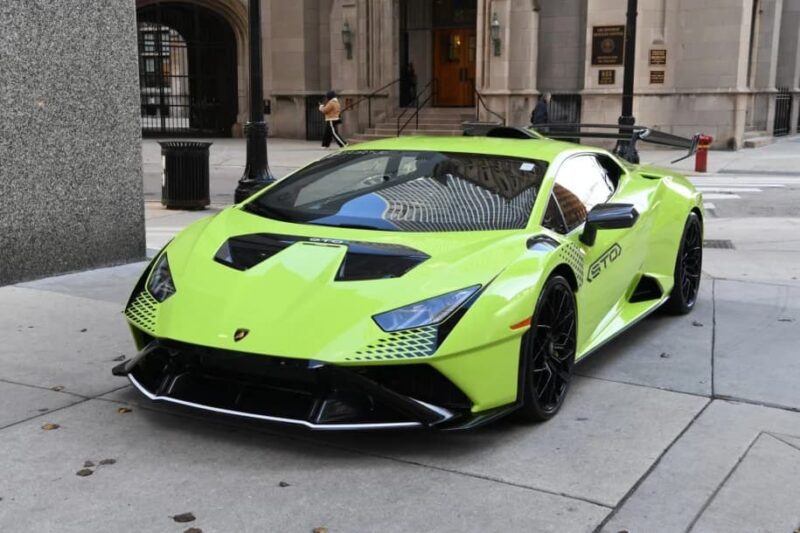 A bright green Lamborghini in striking Verde Scandal is parked on a city sidewalk near tall buildings and a pedestrian, hinting at an exciting story waiting to unfold.