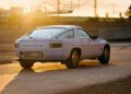 A silver Porsche 928 sports car, one of the rarest colors in its origin story, is parked on a dirt surface at sunset, with shadows cast by the low sun in the background.