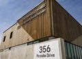A modern building with wooden panels displays the sign "Porsche Experience Centre Toronto," inviting visitors to the ultimate Porsche Experience. A street sign in front reads "356 Porsche Drive.