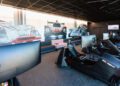 A room at the Toronto Experience Center with Porsche racing car simulators, large monitors, and chairs, set against a wall mural featuring classic race cars.