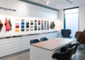 Modern fitting lounge at the Porsche Experience Center, with fabric and leather samples displayed on the wall, a wooden desk with chairs, and two lounge chairs by a large window.