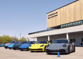 A lineup of six Porsche sports cars in various colors parked outside the Porsche Experience Center Toronto on a sunny day.