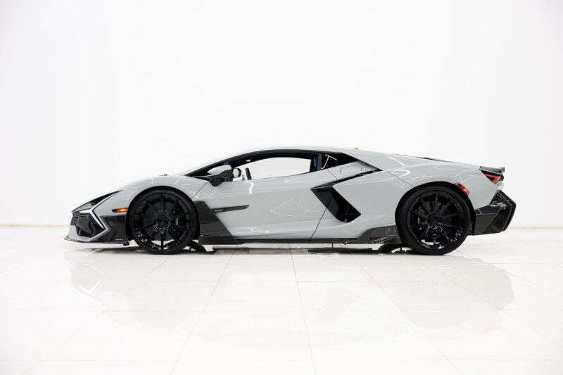 A grey 2025 Mansory Lamborghini Revuelto sports car is parked indoors against a plain white background, viewed from the side, ready to make a statement in the U.S.