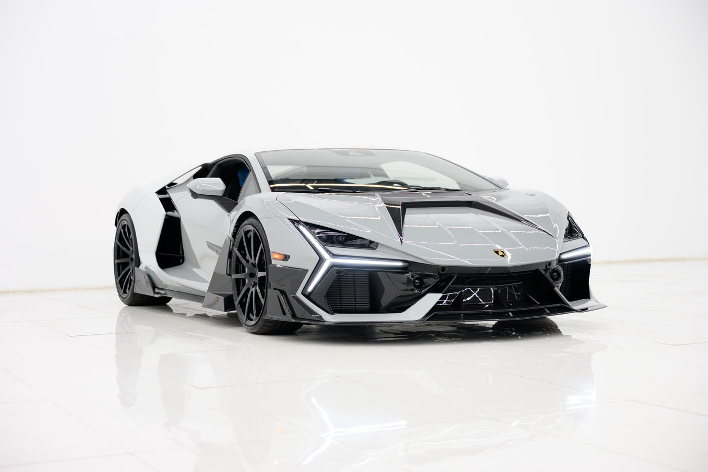 A silver and black 2025 Mansory Lamborghini Revuelto in Limited Spec is displayed in a white, minimalist U.S. showroom with bright lighting.