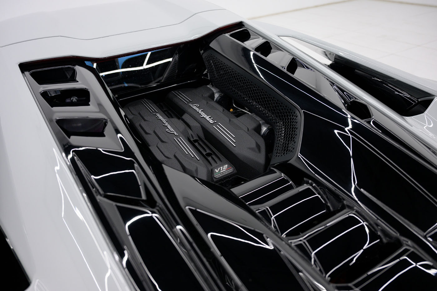 Close-up view of a Mansory Lamborghini Revuelto V12 engine under a glass cover, showcasing sleek black components and glossy white body panels—an exclusive look at the U.S. 2025 model.