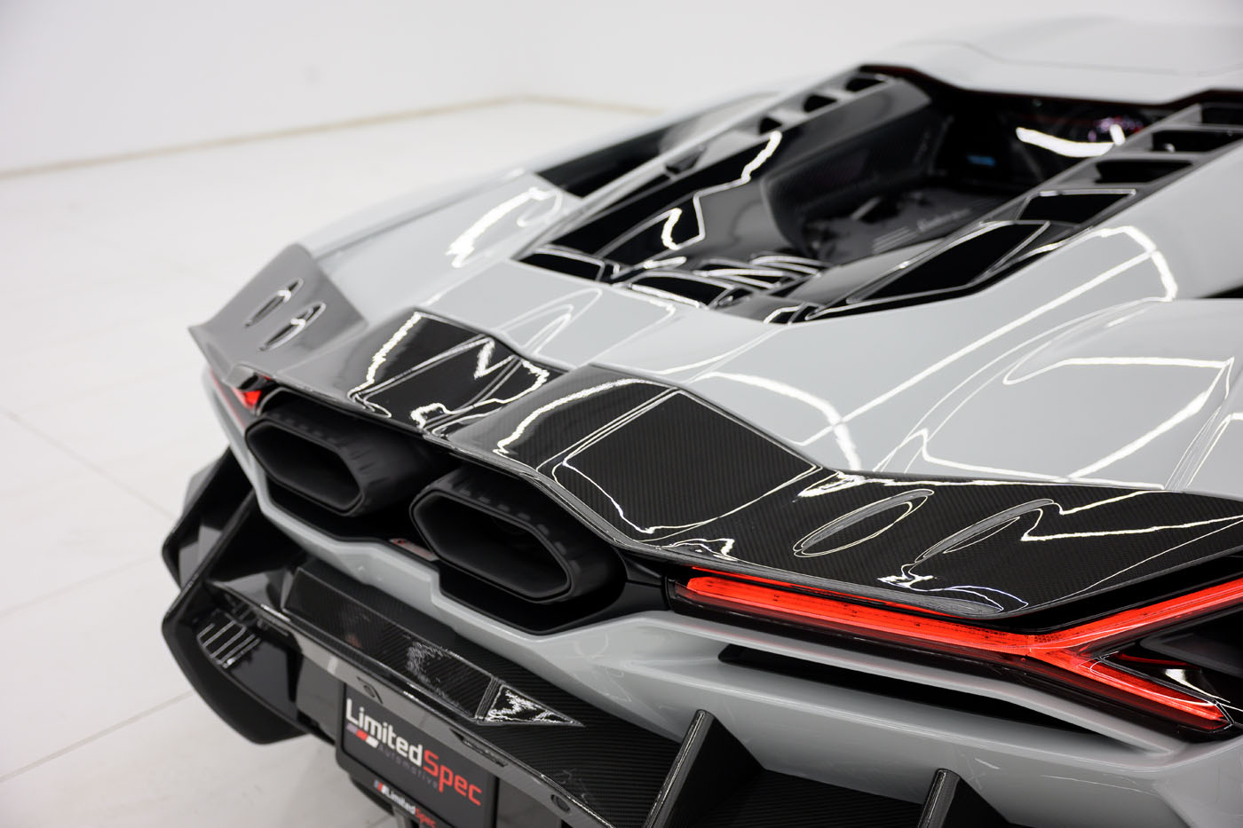Close-up view of the rear end of a 2025 Mansory Lamborghini Revuelto in a U.S. showroom, showcasing dual exhaust pipes, carbon fiber details, and striking red tail lights.