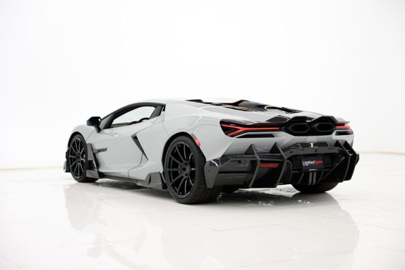 A 2025 Mansory Lamborghini Revuelto sports car viewed from the rear left side, parked indoors on a glossy white floor with a plain white background.