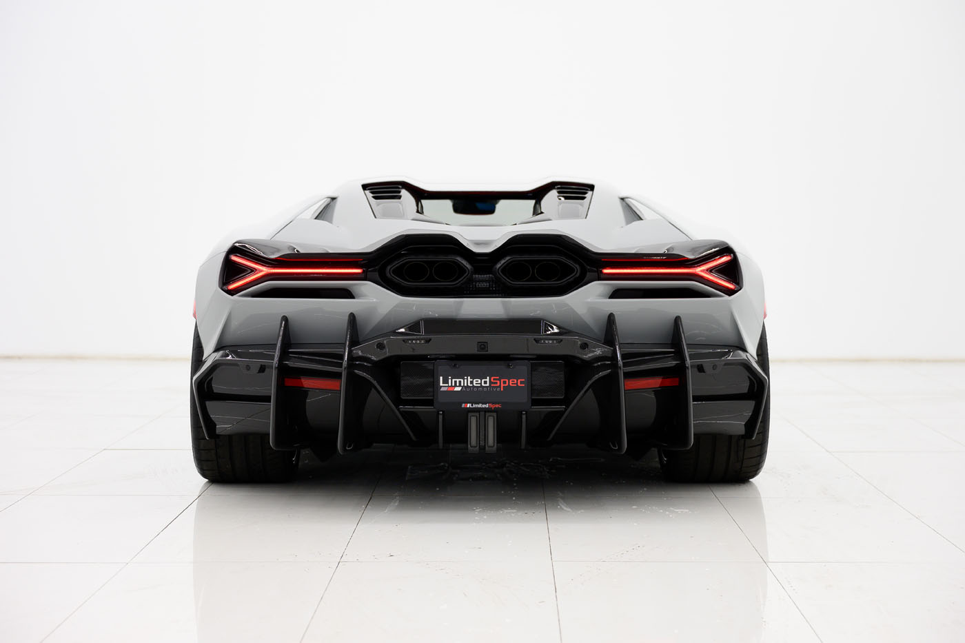 Rear view of a 2025 Lamborghini sports car with distinctive tail lights, dual exhausts, and a prominent rear diffuser, photographed in a clean, white studio setting. This exclusive model evokes the bold spirit of the U.S. Mansory Lamborghini Revuelto.