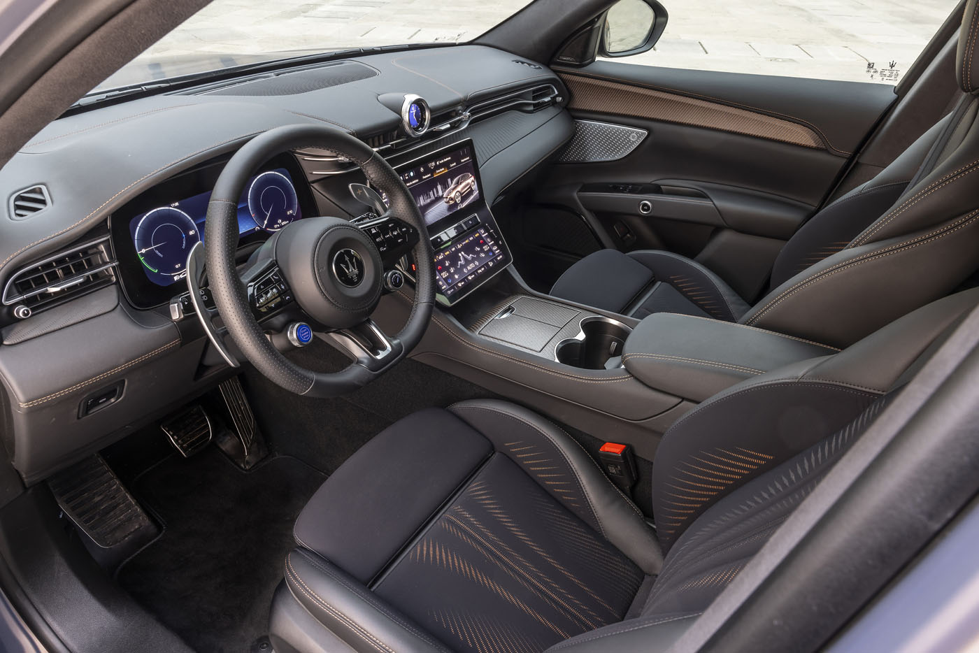 Modern car interior featuring digital displays, a touchscreen center console, black leather seats with orange stitching, and a sporty steering wheel—perfect for cruising the Florida Keys in the all-electric Maserati Grecale Folgore.