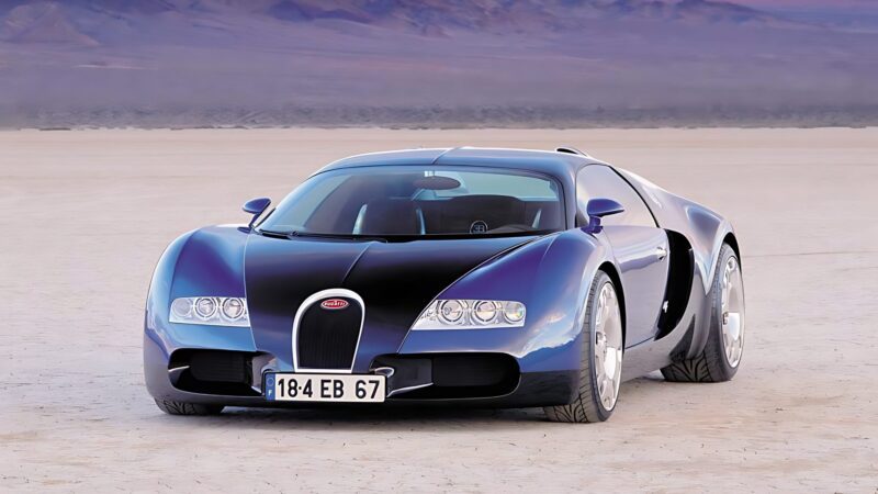 A black and silver sports car, reminiscent of Veyron: The Man The Machine And The Legacy That Rebuilt Bugatti, is parked on a flat, dry desert landscape with mountains in the background.