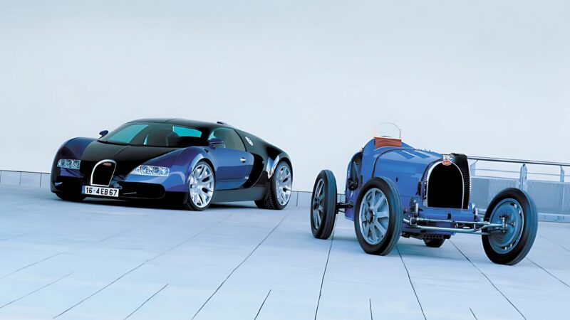 A modern black and blue Bugatti supercar is parked next to a vintage blue Bugatti race car, reflecting the legacy celebrated in Veyron: The Man The Machine And The Legacy That Rebuilt Bugatti.