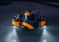 Front view of a black and orange McLaren Le Mans Hypercar with headlights on, driving on a racetrack at night.