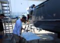 Several people work on and around a docked boat in a marina, with one person handling materials on a table and others standing on ladders next to the hull, demonstrating how Florida boaters care for their vessels and prioritize boat protection.