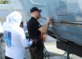 Three people inspect and work on the exterior of an aircraft near an open hangar, with one person using tools to apply Marine Protection Film on the aircraft's surface.