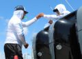 Two Florida boaters in sun-protective clothing handle fishing line near large boat motors under a clear blue sky, likely benefiting from marine protection film to shield their vessel.