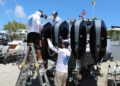 Three people in sun-protective clothing service four large outboard boat engines at a marina, using tools and a ladder—showcasing how Florida Boaters rely on advanced Marine Protection Film for lasting care.