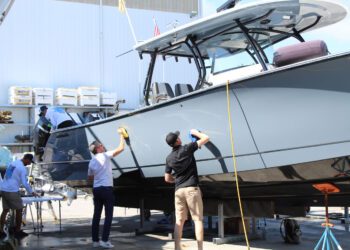 Several people clean and polish a large boat at a dock, with supplies nearby—typical of Florida Boaters who prioritize Marine Protection for their vessels.