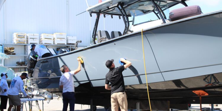 Several people clean and polish a large boat at a dock, with supplies nearby—typical of Florida Boaters who prioritize Marine Protection for their vessels.