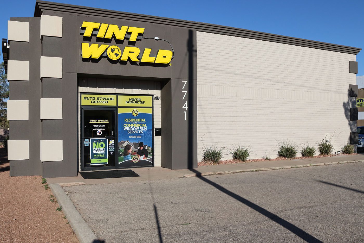 A commercial building with a "Tint World" sign above the entrance and street number 7741 displayed on the front. The entrance door has promotional signs for auto and residential services.