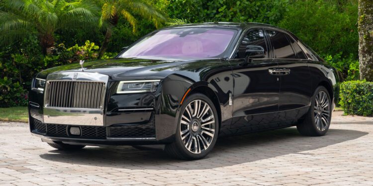 A 2024 Rolls-Royce Ghost collector’s car sedan parked on a stone driveway, surrounded by green foliage and palm trees.