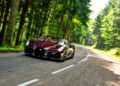 A Bugatti W16 Mistral cruises on a winding road through a forested area near Molsheim, gleaming in the sun on a perfect day.