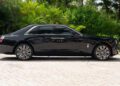 A 2024 Rolls-Royce Ghost luxury sedan is parked on a stone driveway, surrounded by lush green tropical plants and trees—a true collector’s car set in a serene escape.