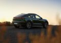 A dark green Porsche Macan SUV is parked on an asphalt road at sunset, viewed from the rear left side with tall grass in the foreground, reflecting Porsche Cars North America’s outlook for H1 2025 growth.