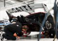 Two technicians from the expert support team work underneath the rear of a raised, exclusive Bugatti Bolide in a brightly lit garage.