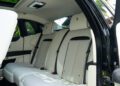 The image shows the rear seats of a 2024 Rolls-Royce Ghost with white leather upholstery, black accents, and headrests featuring an embroidered logo.