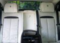 The image shows the rear seats of a 2024 Rolls-Royce Ghost, featuring white leather upholstery with black seat belts and headrests bearing the Rolls-Royce logo—a true collector’s car interior.