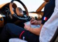 A person sits in the driver's seat of a Bugatti W16 Mistral, writing on a notepad as they prepare to test the luxury car—its sleek dashboard and signature Molsheim craftsmanship on display.