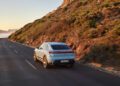 A silver Porsche Macan drives along a coastal road at sunset, with rocky cliffs and the ocean in the background—a stunning scene for H1 2025 Porsche cars.