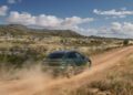 A green Macan SUV drives on a dusty dirt road through a rocky, grassy landscape under a partly cloudy sky—showcasing the adventure-ready spirit of Porsche Cars.