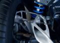 Close-up of a Bugatti car’s suspension system featuring a blue coil spring, tire, and a metallic control arm with a complex, lightweight structure.