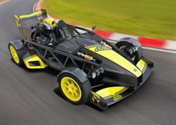 A black and yellow Ariel Atom 4RR with 525HP and an exposed frame speeds along a racetrack, steered by a helmeted driver.