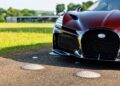 Front close-up view of a red Bugatti W16 Mistral with a prominent grille, parked on pavement near a grassy area and modern building in the background, embodying the innovative spirit of Molsheim.