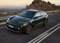 A green Porsche Macan from Porsche Cars North America drives on a winding road with rocky hills and a scenic landscape in the background, showcasing the excitement of H1 2025.