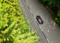 Aerial view of a red Bugatti W16 Mistral convertible driving on a two-lane road bordered by dense green trees near Molsheim on a sunny day.