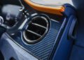 Close-up of a Bentley car air vent set in a carbon fiber dashboard panel, with orange stitching detail visible on the upper trim—a hallmark of the Mulliner Interior luxury car craftsmanship.