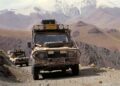 Two off-road vehicles travel on a rough mountain road with snow-capped peaks in the background during the Camel Trophy expedition, echoing the spirit of Land Rover Classic to Showcase 10 Historic Expedition Icons at 2025 Pebble Beach Concours d'Elegance.